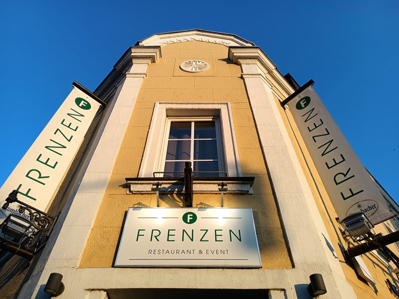 Fassade des Hauses mit dem FRENZEN-Schriftzug über dem Eingang, von unten fotografiert bei Abendlicht