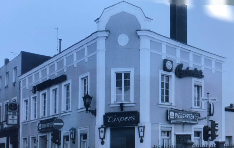 Das Haus Caspers an der Straßenecke mit dem Schriftzug „Caspers“ und Biergarten-Schildern an der Fassade, aufgenommen bei Abendlicht