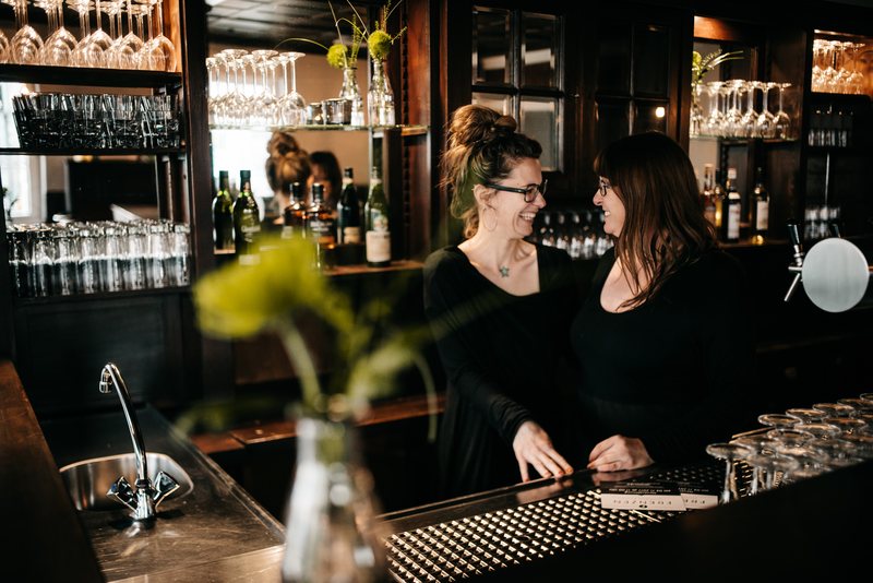Zwei Kolleginnen lachen hinter dem Tresen des TILL